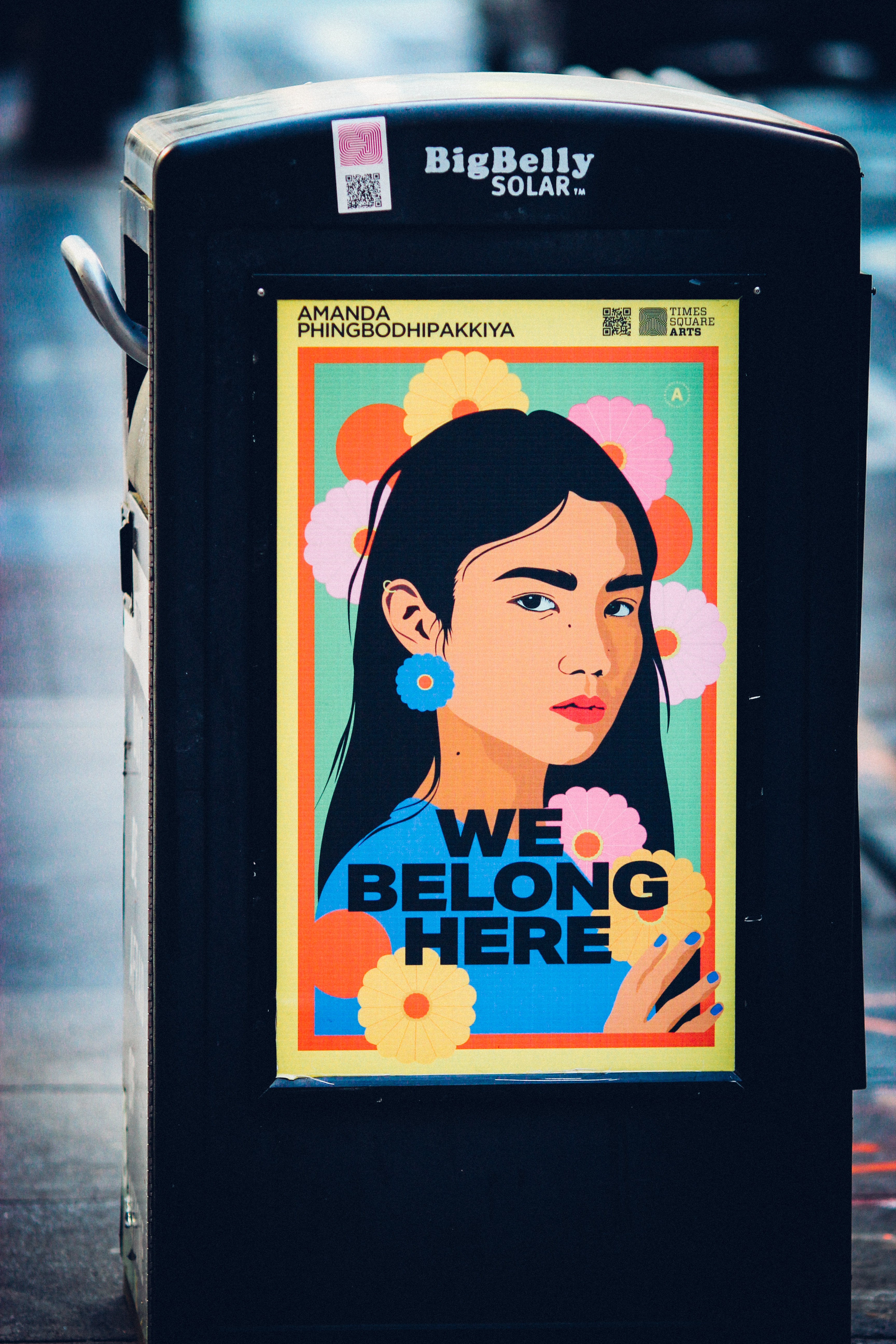 Flyer on a trash can with an Asian American women and text that says 'We Belong Here.'